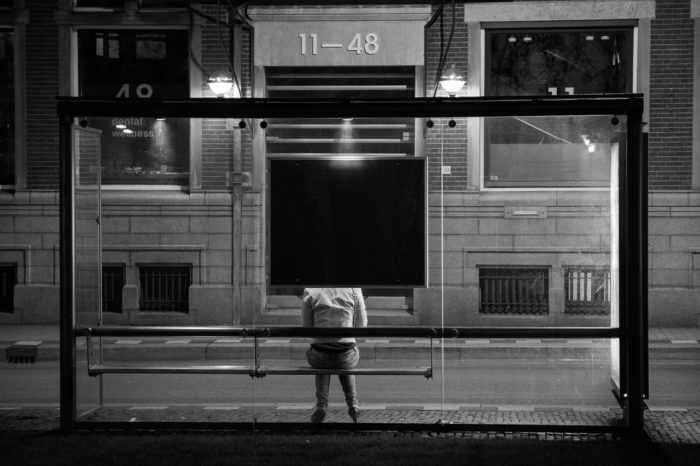 black and white of man sitting at bus stop